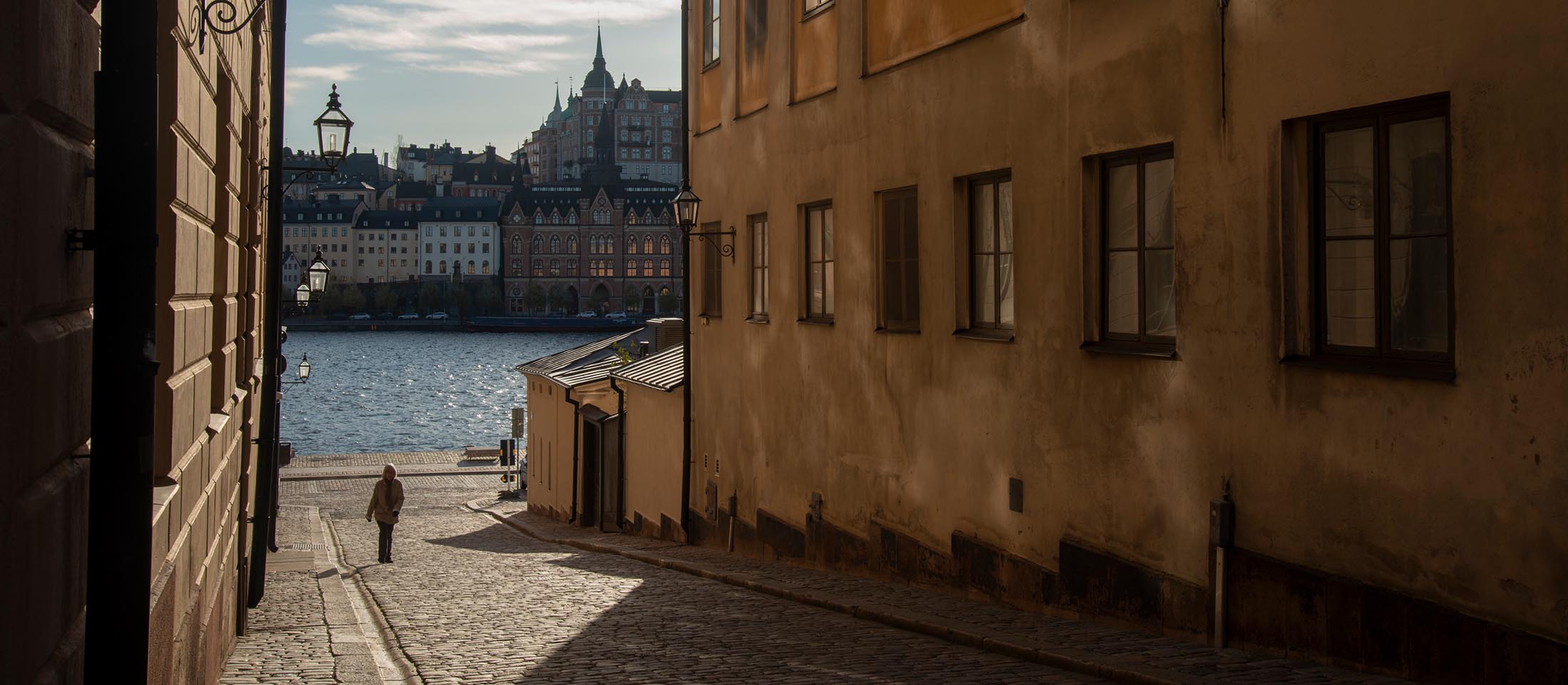 Stockholm-Sweden-Riddarholmen-ELJ-012-banner A pedestrian walks on a cobblestone street, at Riddarholmen, Stockholm, Sweden. Photo by Eva-Lotta Jansson